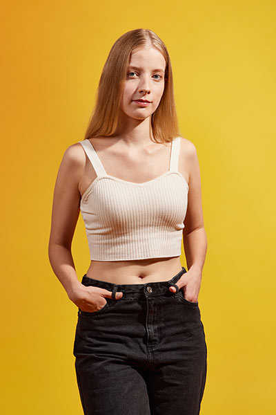 Eine junge Frau mit bauchfreiem Top und Jeans schaut seitwärts in die Kamera.