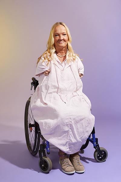 Eine Frau mit blondem Haar und rosa Kleid blickt selbstbewusst nach Vorne.