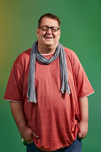 Ein großer Mann mit Brille und Schal lacht mit geschlossenen Augen authentisch. 